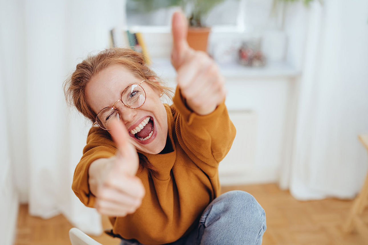 Junge Frau mit Brille zeigt zwei Daumen hoch und freut sich über das Festgeld