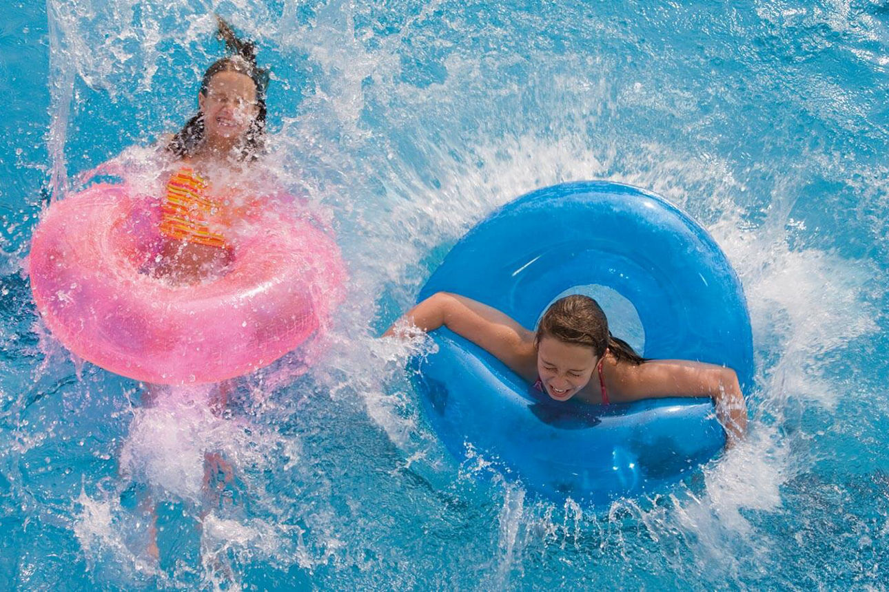 Zwei Mädchen genießen das frische Wasser im Swimmingpool in einem Schwimmring