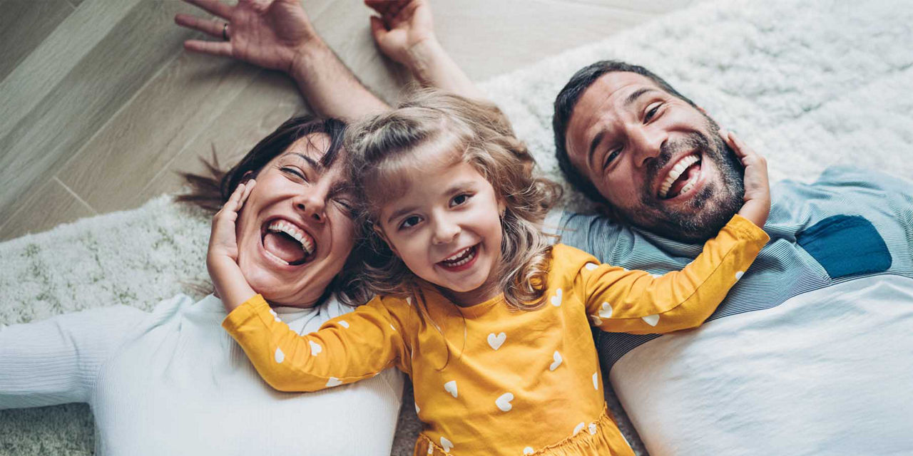 Junges Paar liegt lachend mit ihrer Tochter auf dem Boden