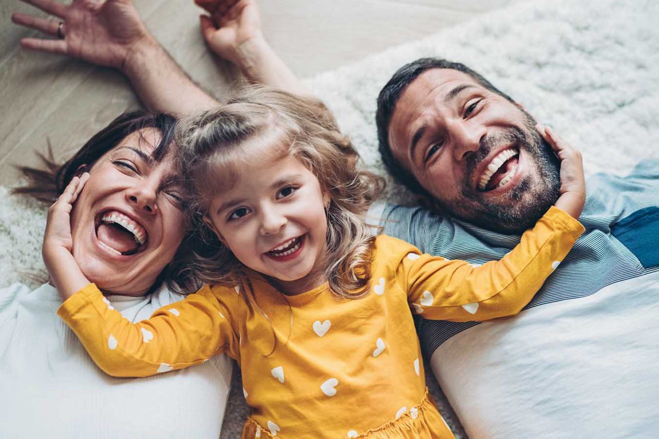 Junges Paar liegt lachend mit ihrer Tochter auf dem Boden