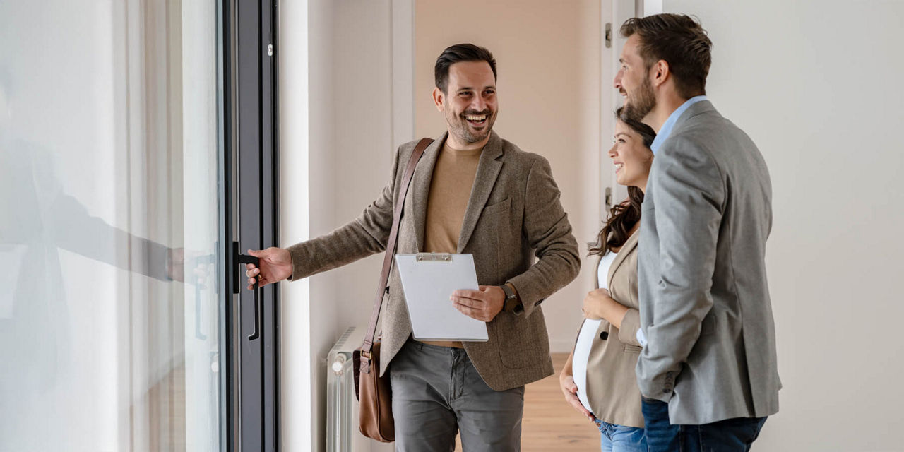 Junges Paar lacht zusammen mit dem Immobilienmakler während einer Besichtigung