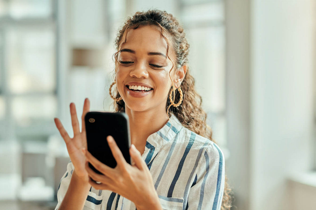 Junge Frau schaut lächelnd auf ihr Handy