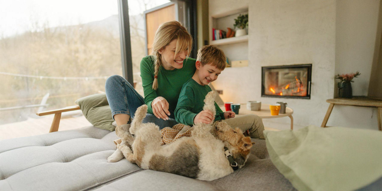Junge Mutter und Sohn spielen mit dem Hund. Im Hintergrund knistert der Kamin
