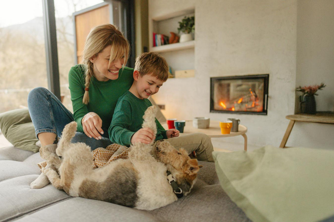 Junge Mutter und Sohn spielen mit dem Hund. Im Hintergrund knistert der Kamin