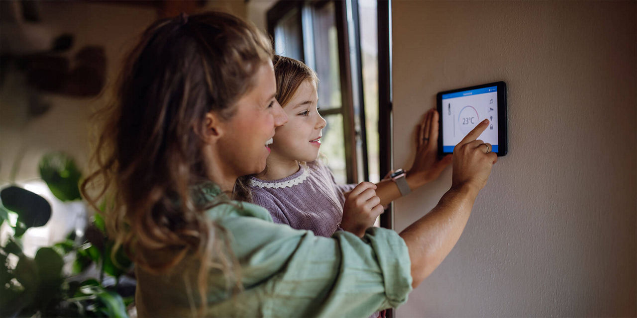Frau mit Kind auf dem Arm nutzt digitales Thermostat 