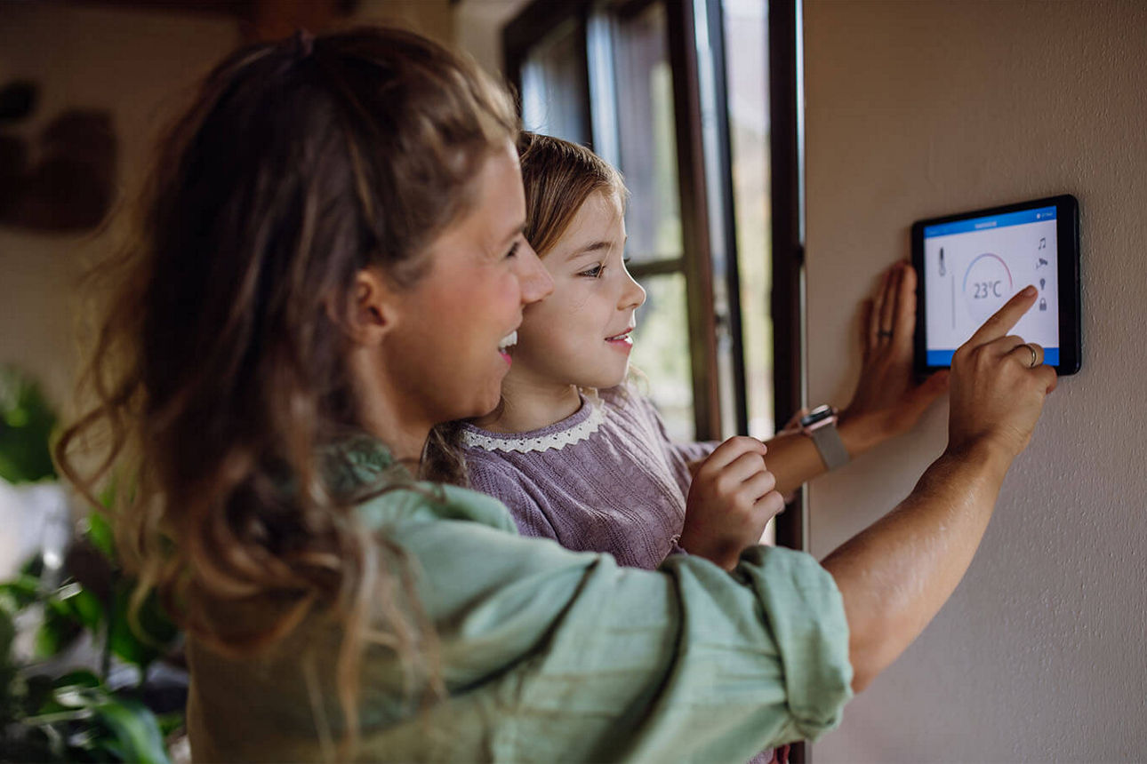 Frau mit Kind auf dem Arm nutzt digitales Thermostat 