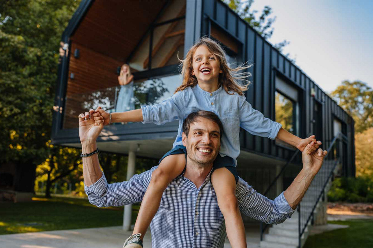 Ein junger Vater spielt fröhlich mit seiner Tochter vor dem eigenen Haus