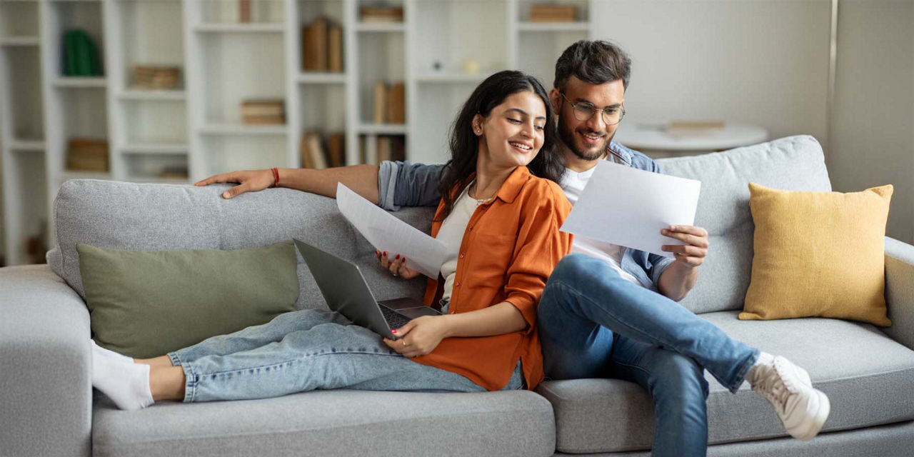 Ein junges Paar sitzt glücklich auf dem Sofa während sie Dokumente besprechen