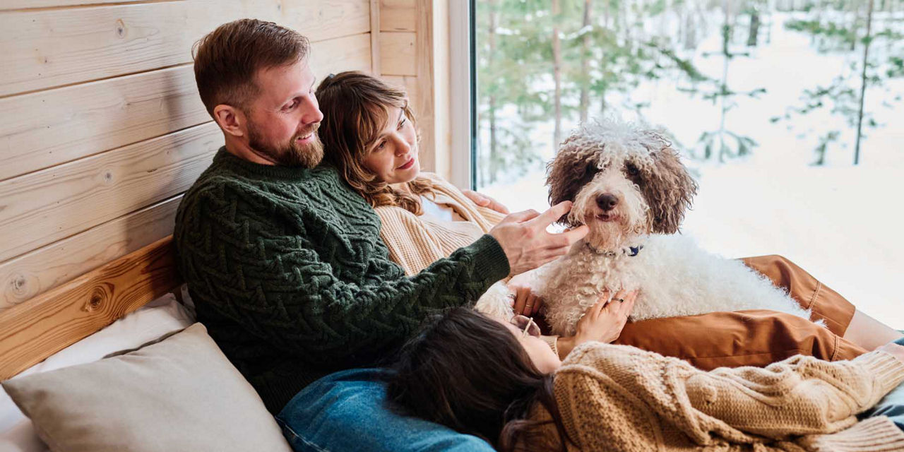 Eine junge Familie liegt im Winter gemütlich mit ihrem Hund im Bett