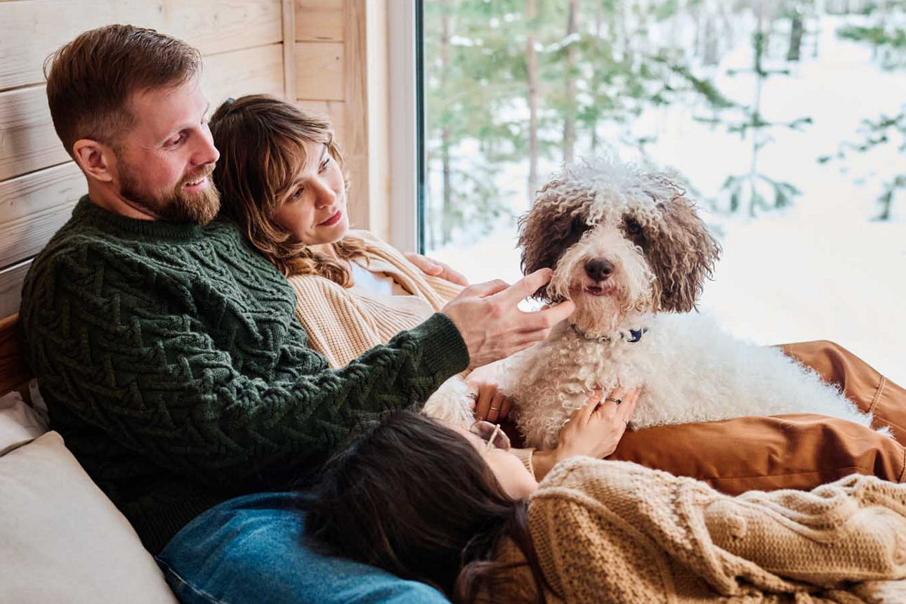 Eine junge Familie liegt im Winter gemütlich mit ihrem Hund im Bett