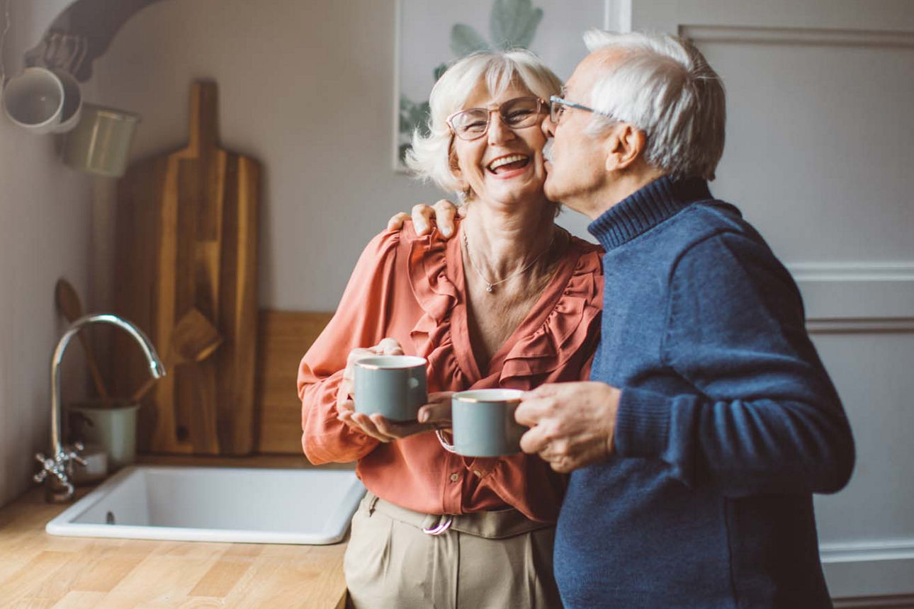 Ein glückliches älteres Paar steht in der Küche und trinkt Kaffee