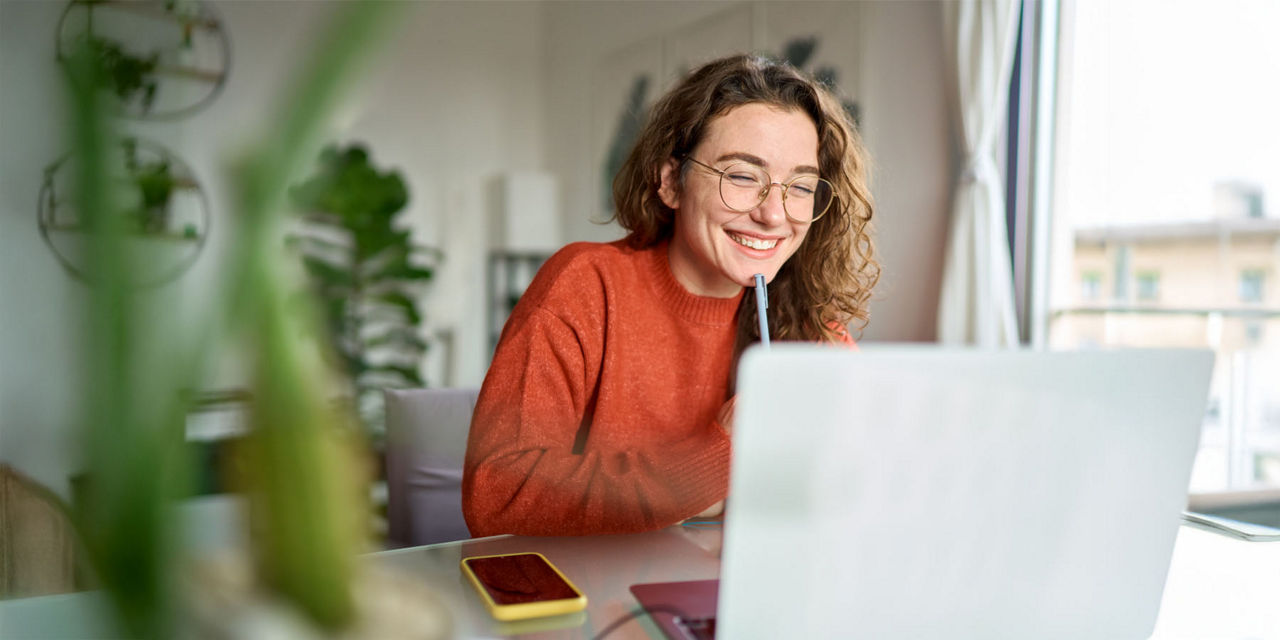 Junge Frau sitzt zufrieden lächelnd vor ihrem Laptop