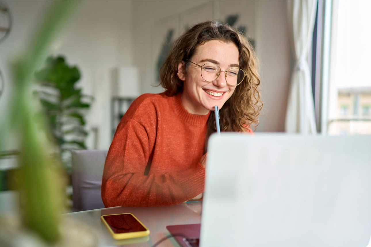 Junge Frau sitzt zufrieden lächelnd vor ihrem Laptop
