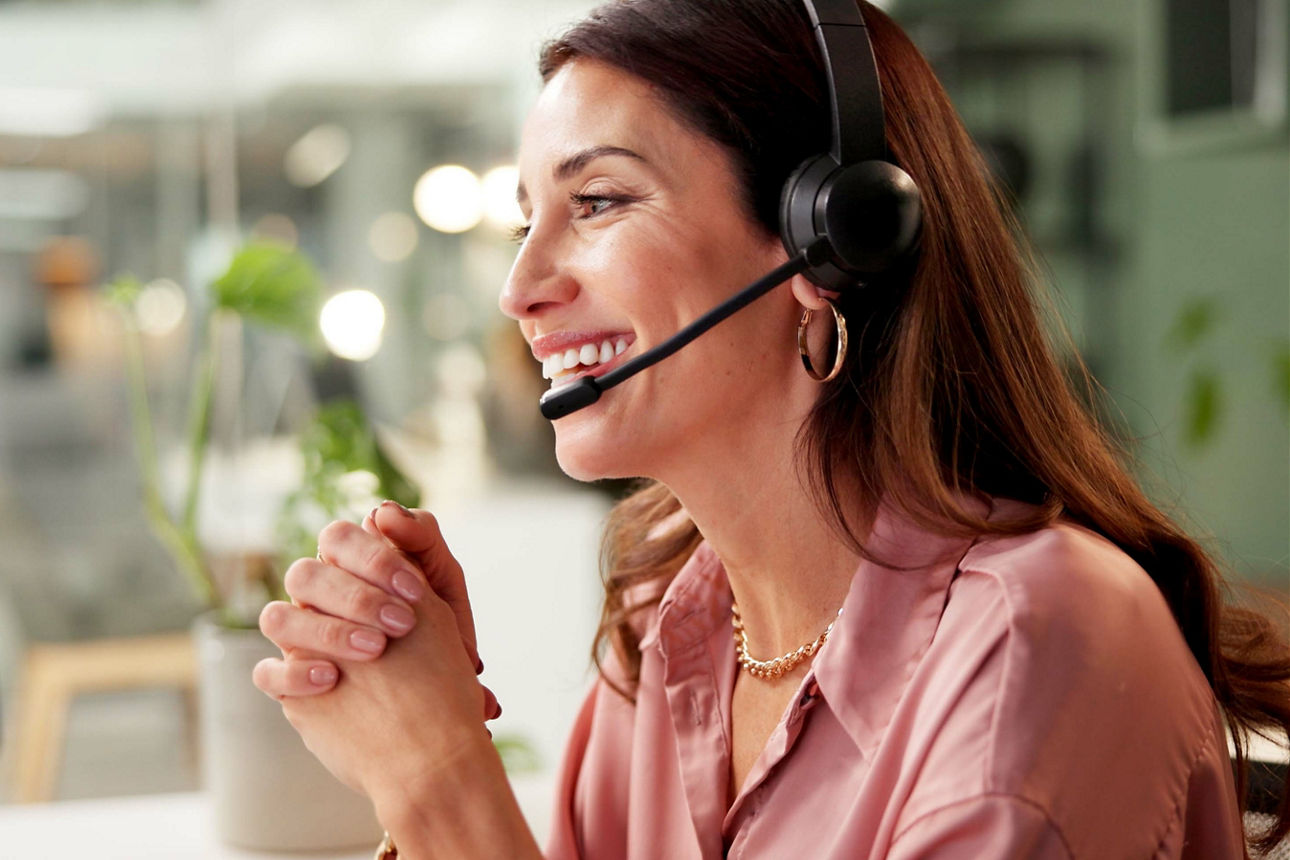 Eine Frau mit Headset sitzt vor einem Bildschirm und lacht