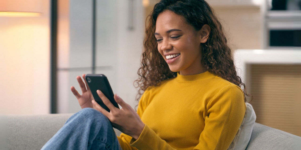 Junge Frau sitzt auf dem Sofa und schaut auf ihr Handy
