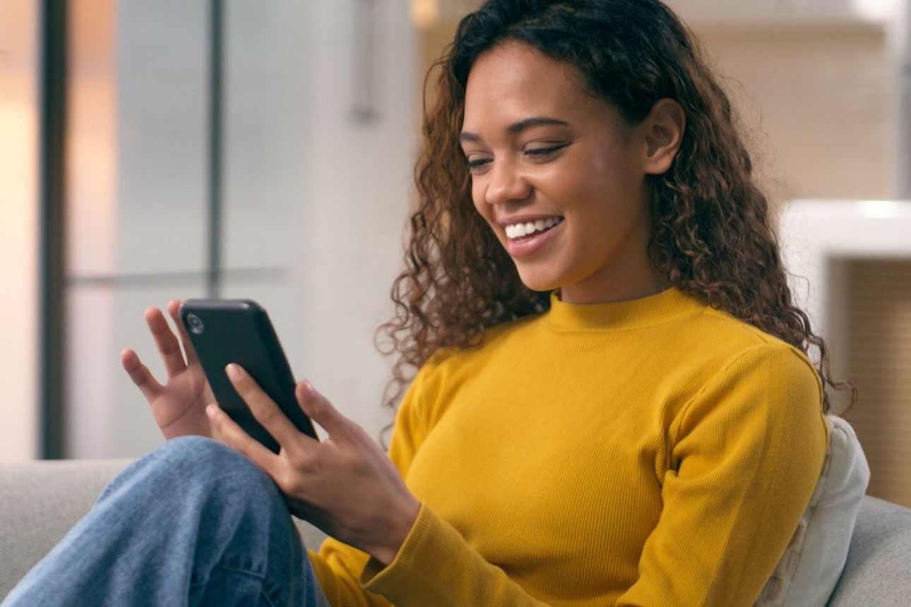 Junge Frau sitzt auf dem Sofa und schaut auf ihr Handy