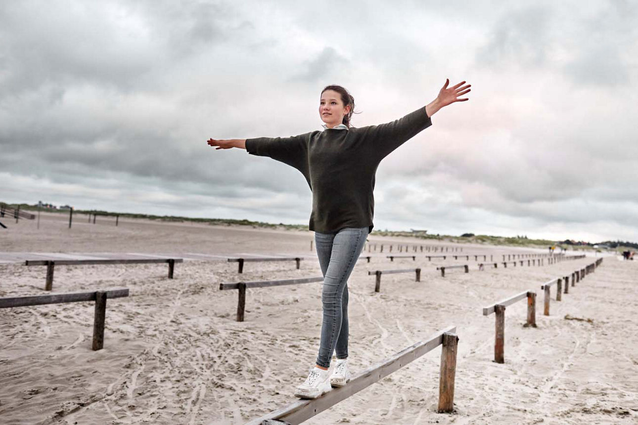 Mädchen im Teenageralter balanciert am Strand über ein Geländer