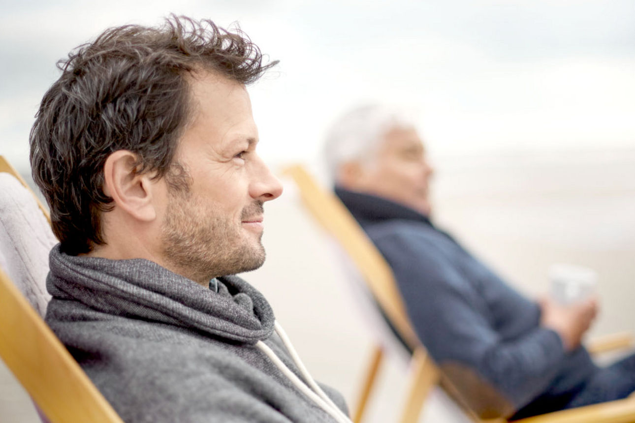 Vater und Sohn sitzen am Strand im Liegestuhl und trinken eine Tasse Kaffee