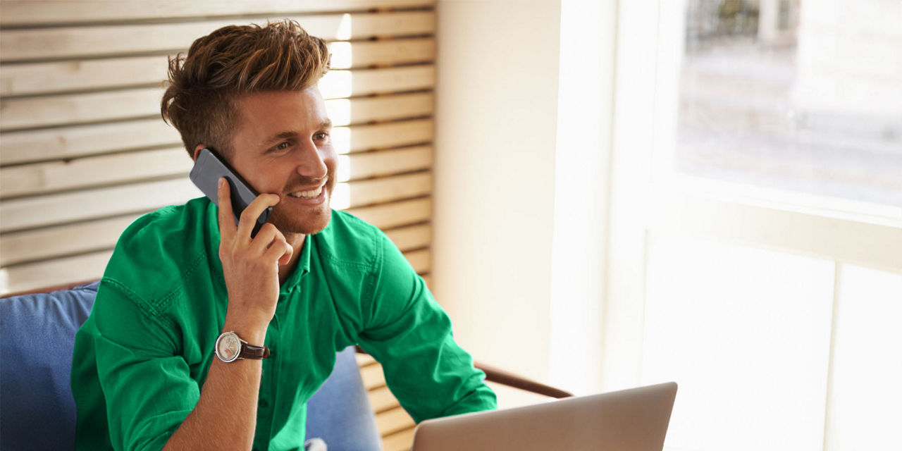 Junger Mann am Tisch sitzend mit Smartphone  und Laptop