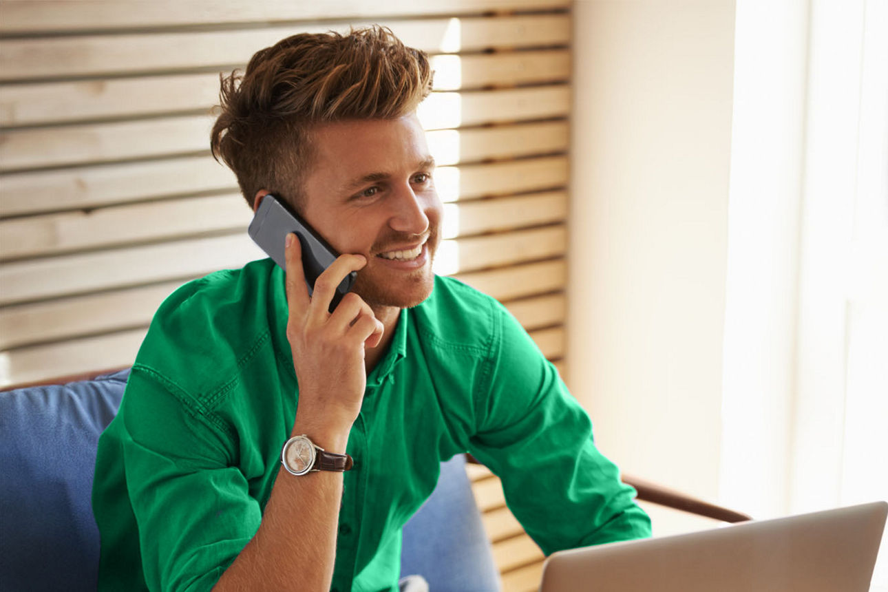 Junger Mann am Tisch sitzend mit Smartphone  und Laptop