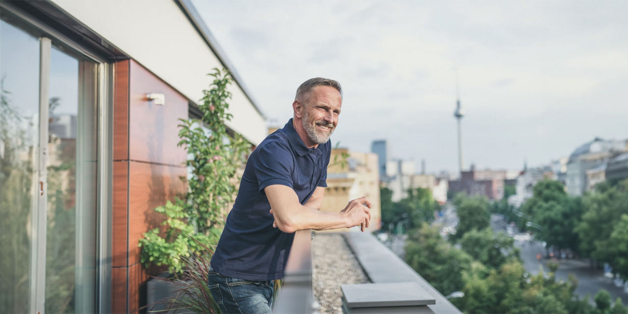 Mann im blauen Poloshirt steht auf eigenem Balkon und blickt auf den Fernsehturm