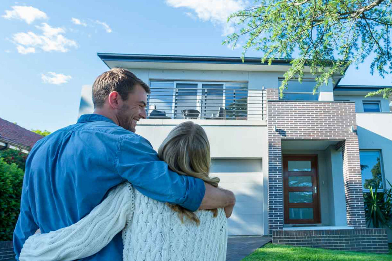 Glückliches Ehepaar steht Arm in Arm vor dem freistehenden Einfamilienhaus 