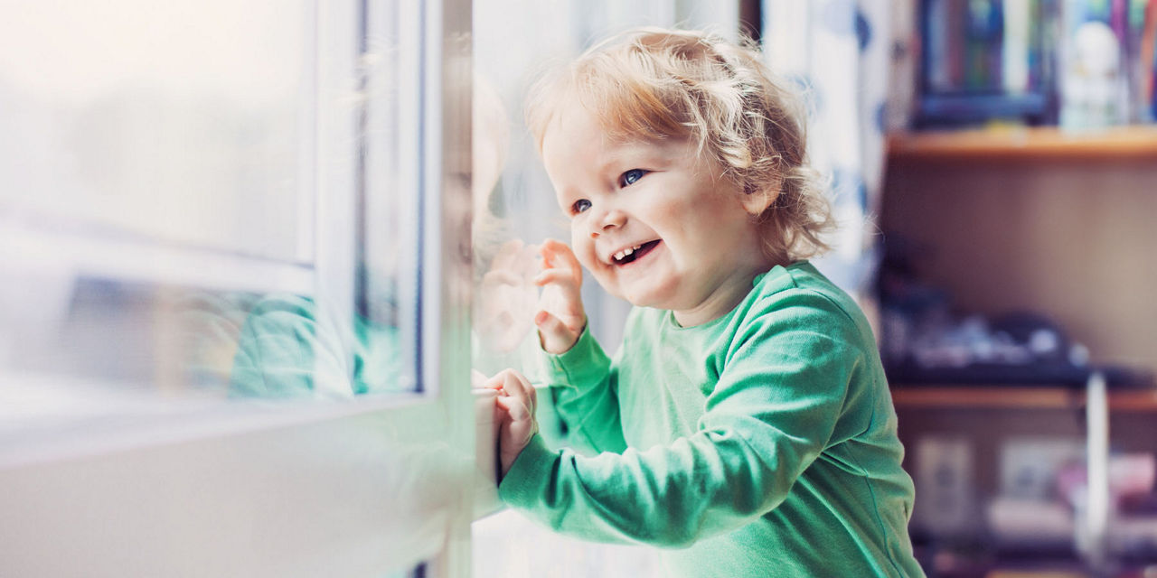 Junges Mädchen sitzt im Kinderzimmer und schaut durch die Fenster nach Draußen