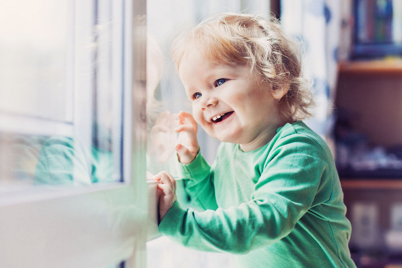 Junges Mädchen sitzt im Kinderzimmer und schaut durch die Fenster nach Draußen