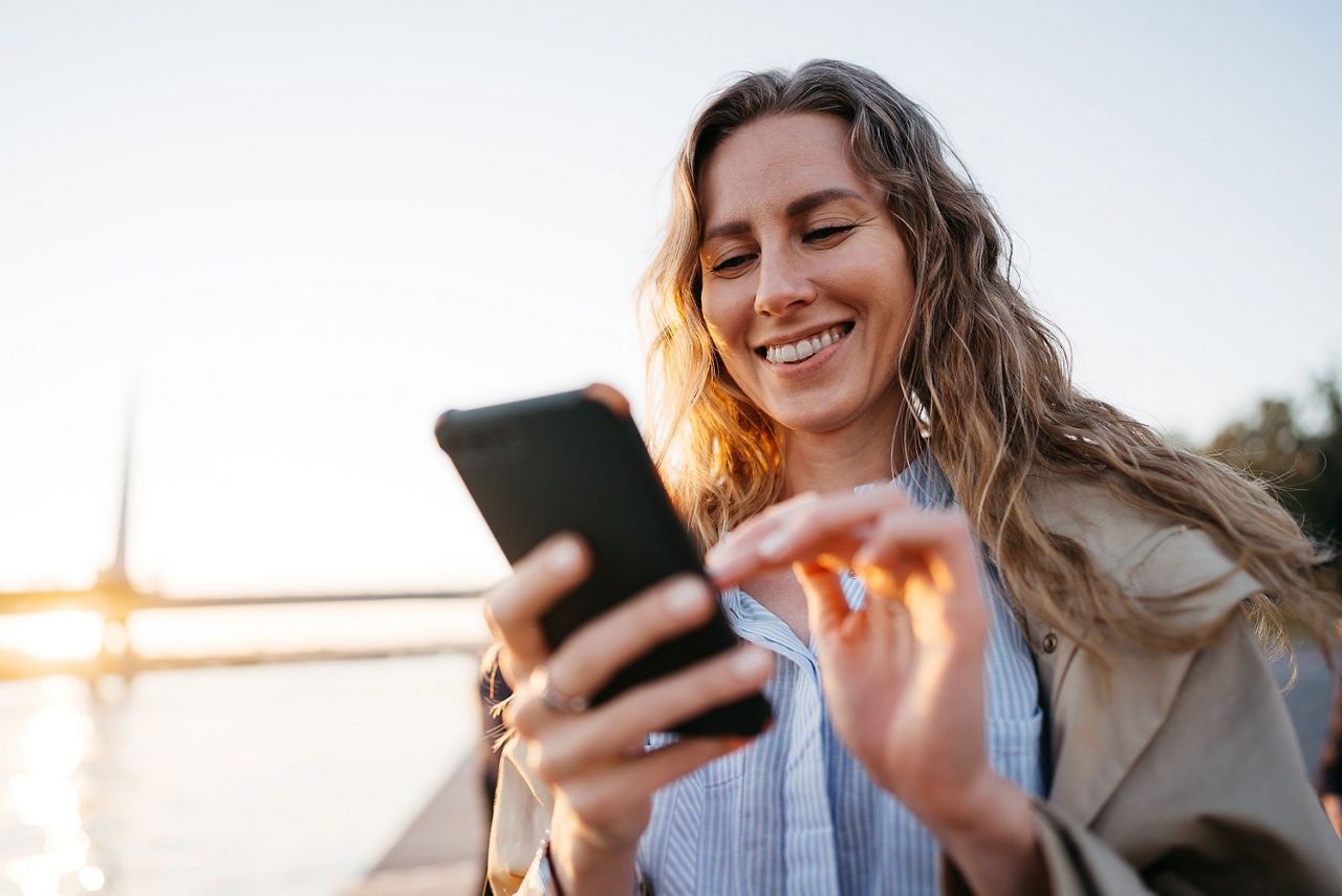 Eine Frau läuft draußen mit Ihrem Handy in der Hand und lächelt in ihr Handy.