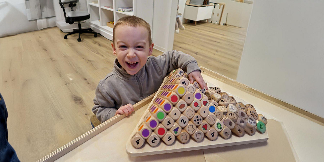 Kleiner Junge spielt in einer Kita mit einem Würfelset und freut sich