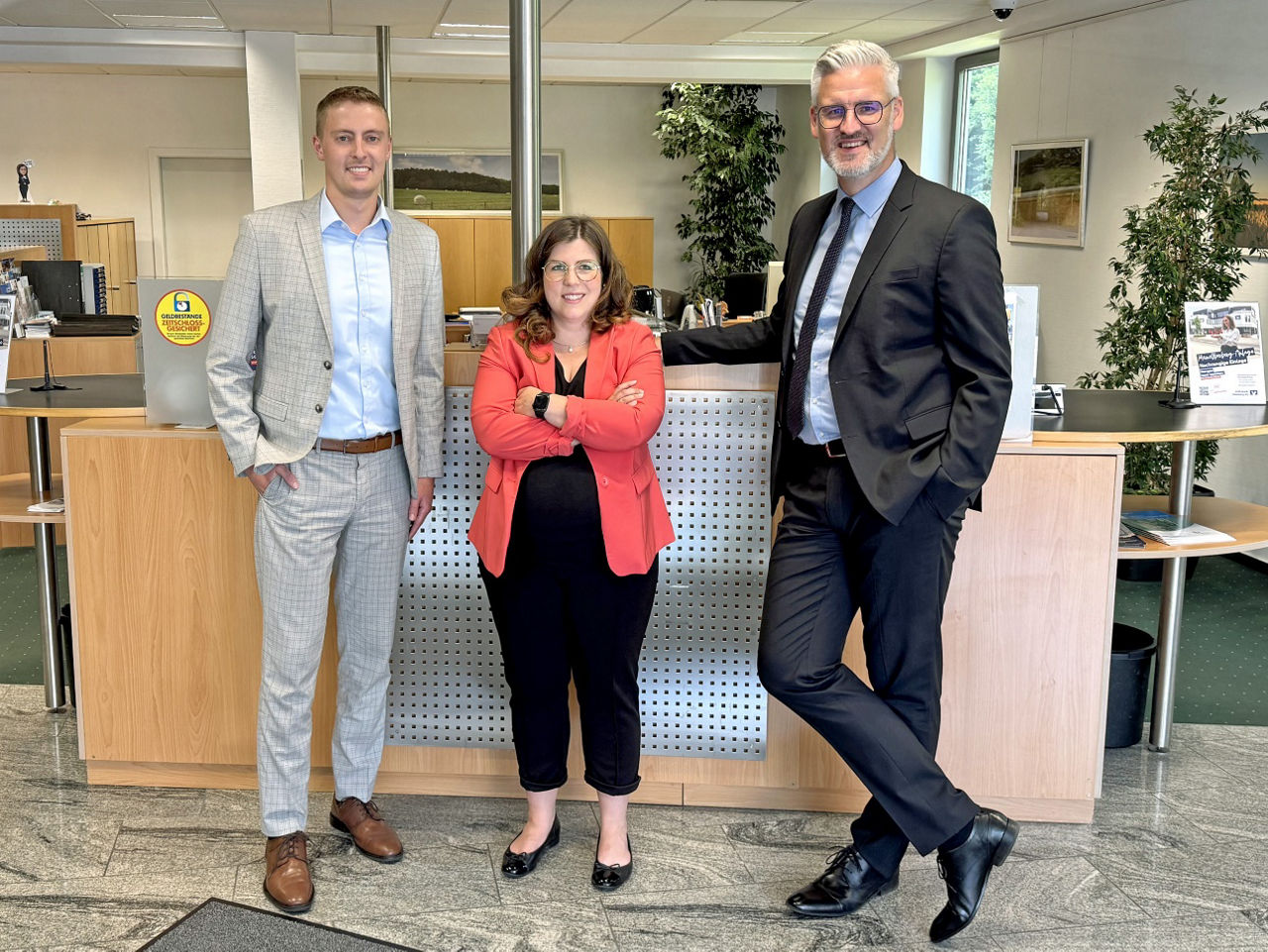 Drei Personen vor dem Bankschalter der Volksbank-Geschäftsstelle Brüchermühle: Tom Schwanbeck (links), Anna-Lena Zauner (Mitte), Sebastian Bender (rechts).