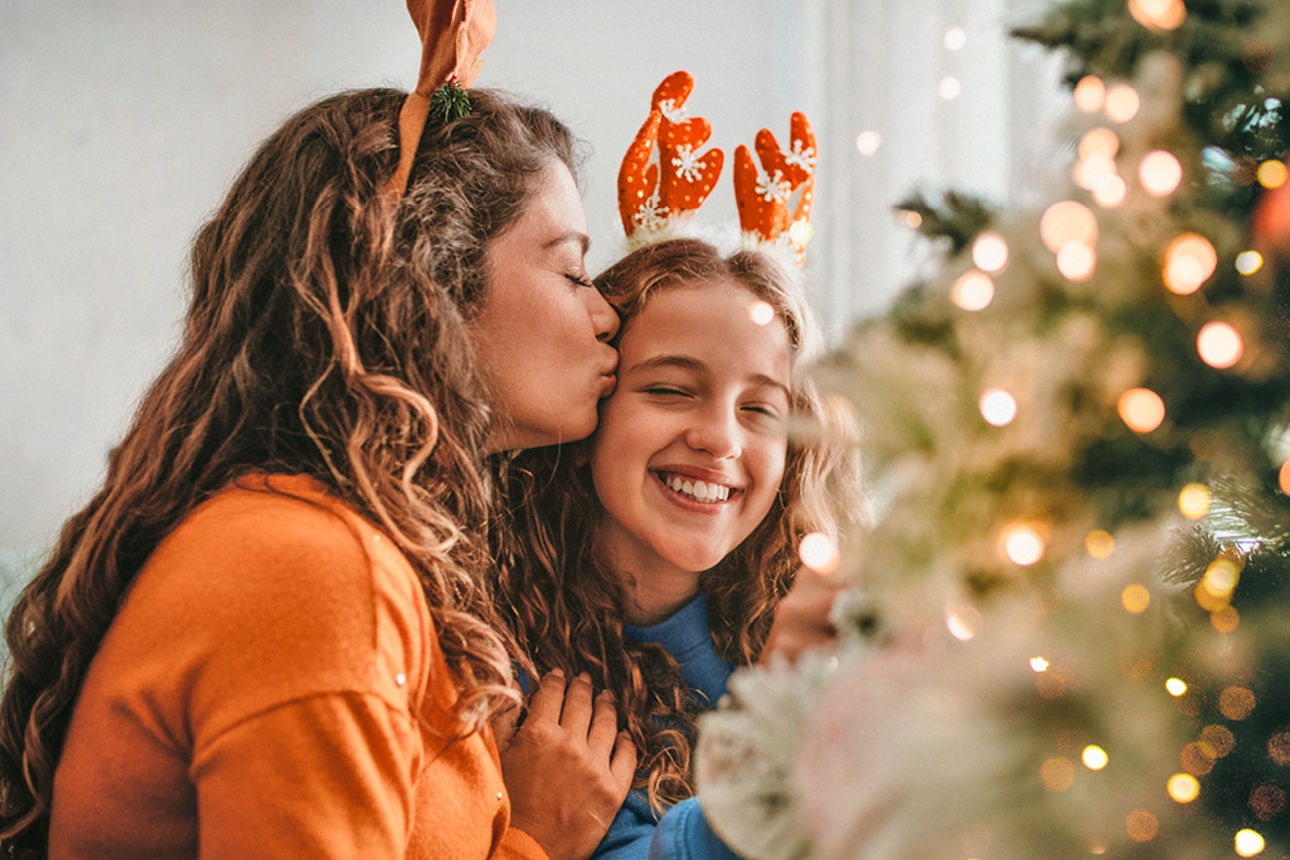 Frau küsst Tochter auf die Stirn neben einem Weihnachtsbaum