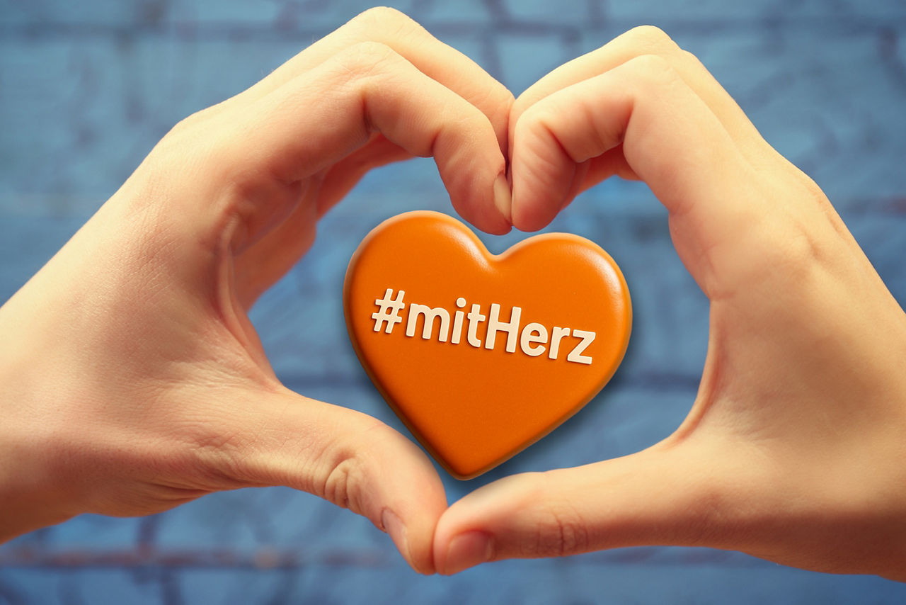 Zwei Hände zeigen ein Herz und in der Mitte ein orangenes Herz mit der Aufschrift #mitHerz