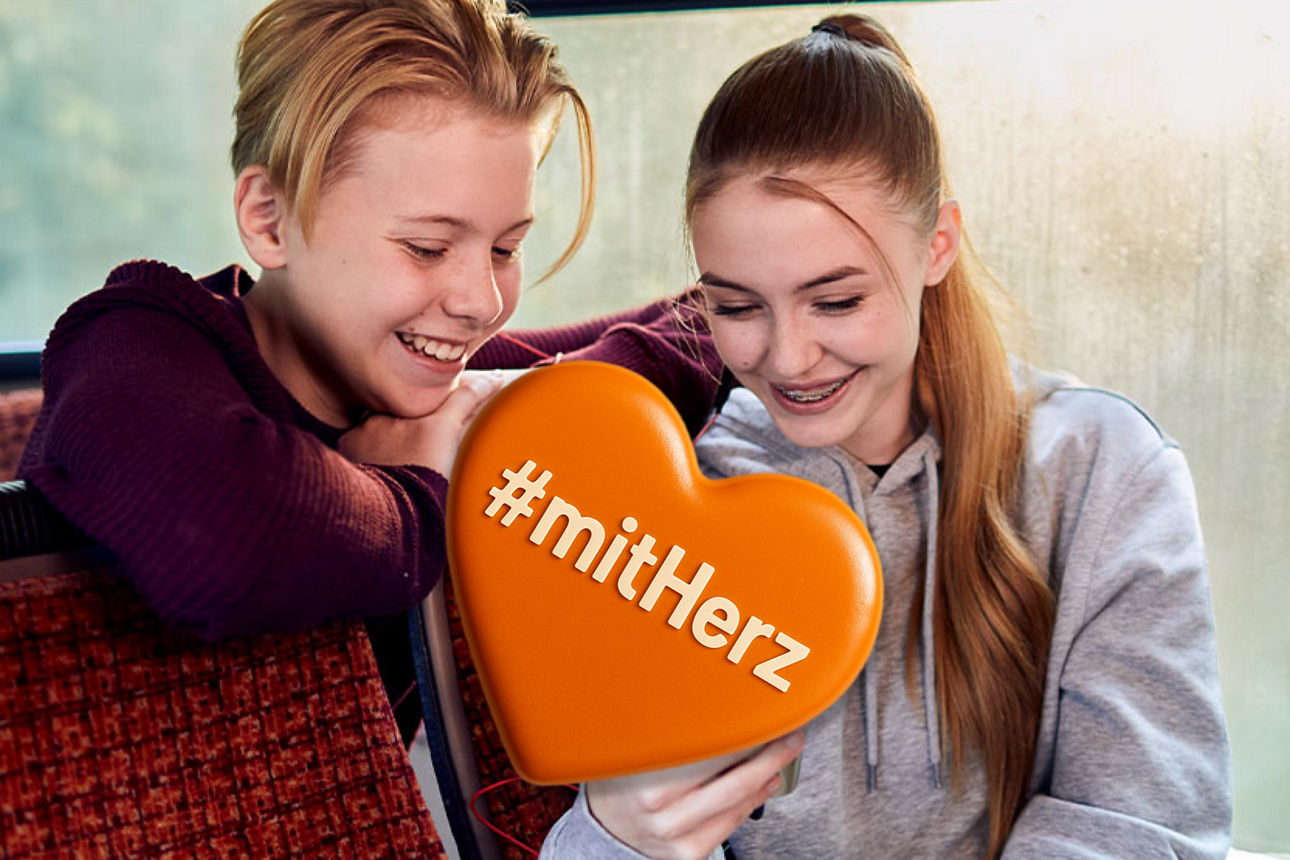 Zwei Jugendliche die in einem Bus sitzen und lachend auf ein Handy schauen in der Mitte #mitHerz