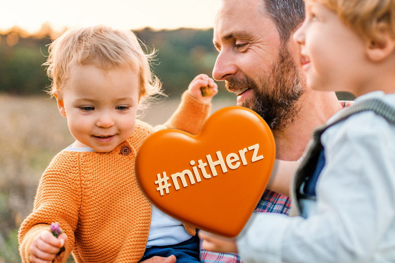 Ein Vater hat seine zwei Kinder auf dem Arm und läuft bei Sonnenuntergang übers Feld
