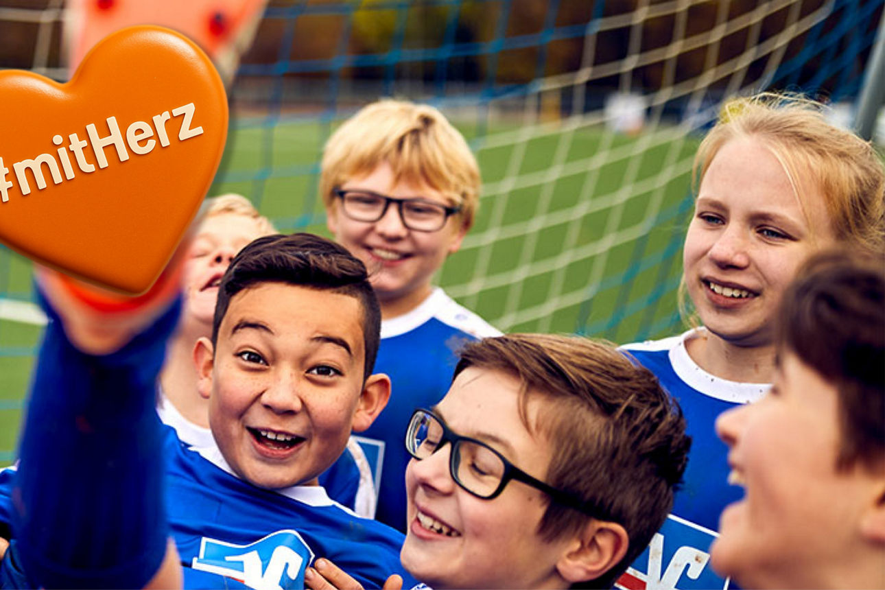 Ein Junge mit Fußballschuhen und Fußballtrikot wird von seiner Mannschaft hochgehoben