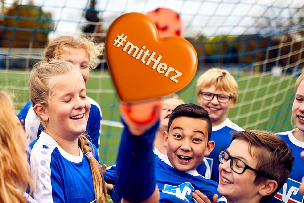 Junge in Fußballkleidung wird von seiner Mannschaft getragen und hebt den Fuß in die Luft #mitHerz