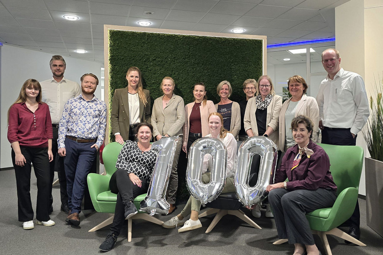 Das Team der Niederlassung Radevormwald lächelt und hält eine 100 aus Luftballons in die Höhe.
