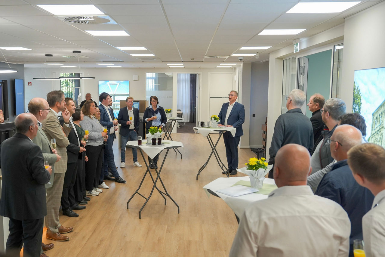 Das Foto zeigt eine Gruppe von Menschen in der neuen Volksbank Filiale in Büderich, die dem Vorstand bei einer Rede zuhören.