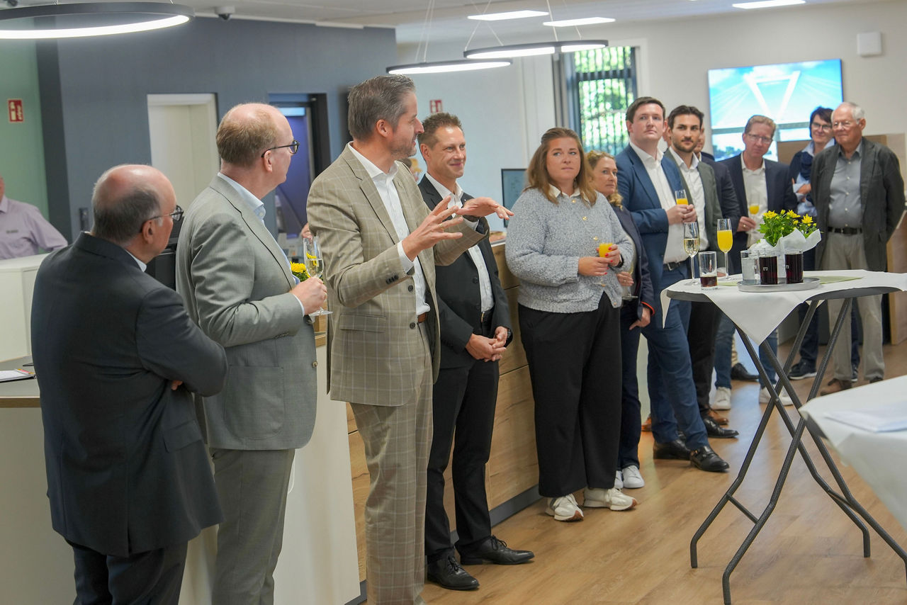 Das Foto zeigt eine Gruppe von Menschen in der neuen Volksbank Filiale in Büderich, die um einen Stehtisch herumstehen.