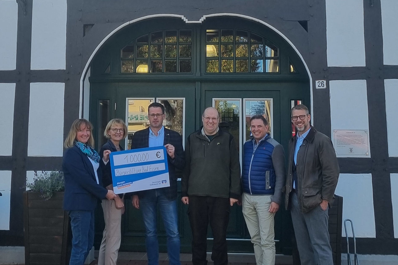 Gruppe vor Volksbank-Gebäude mit Spendenscheck, gemeinsames Foto im Außenbereich