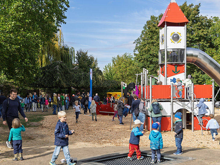 Spielende Kinder und Erwachsene bei strahlendem Sonnenschein auf einem Spielplatz