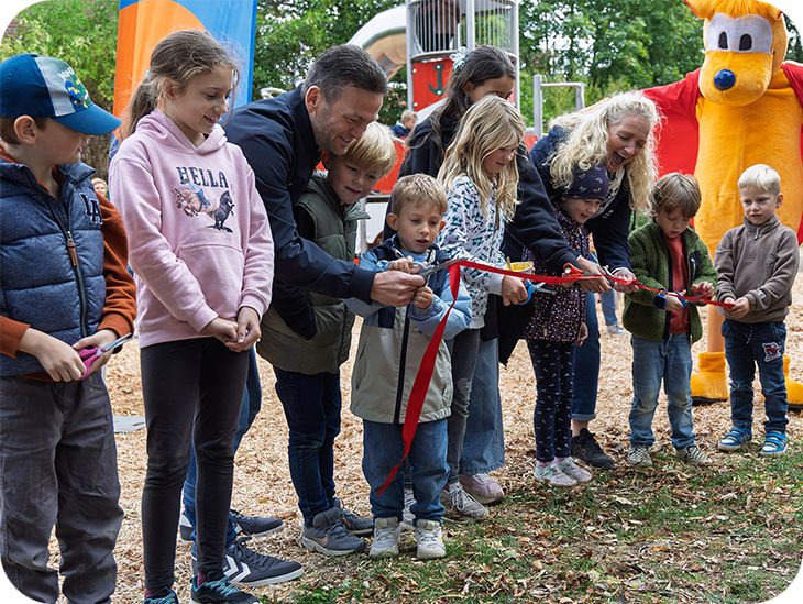 Erwachsene und Kinder auf Spielplatz durchtrennen gemeinsam ein rotes Band