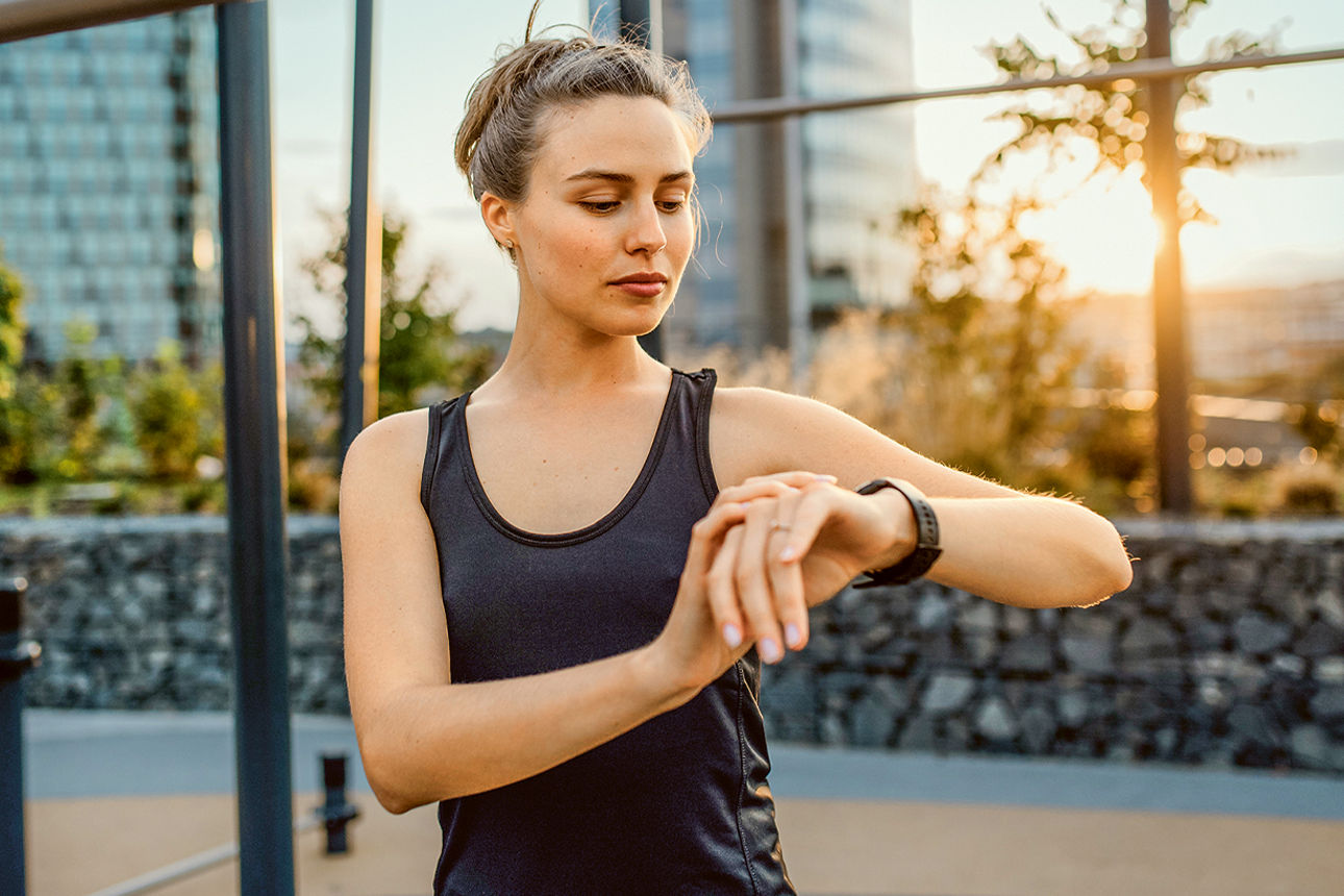 Frau in Sportkleidung steht draußen und schaut auf ihre Smartwatch.