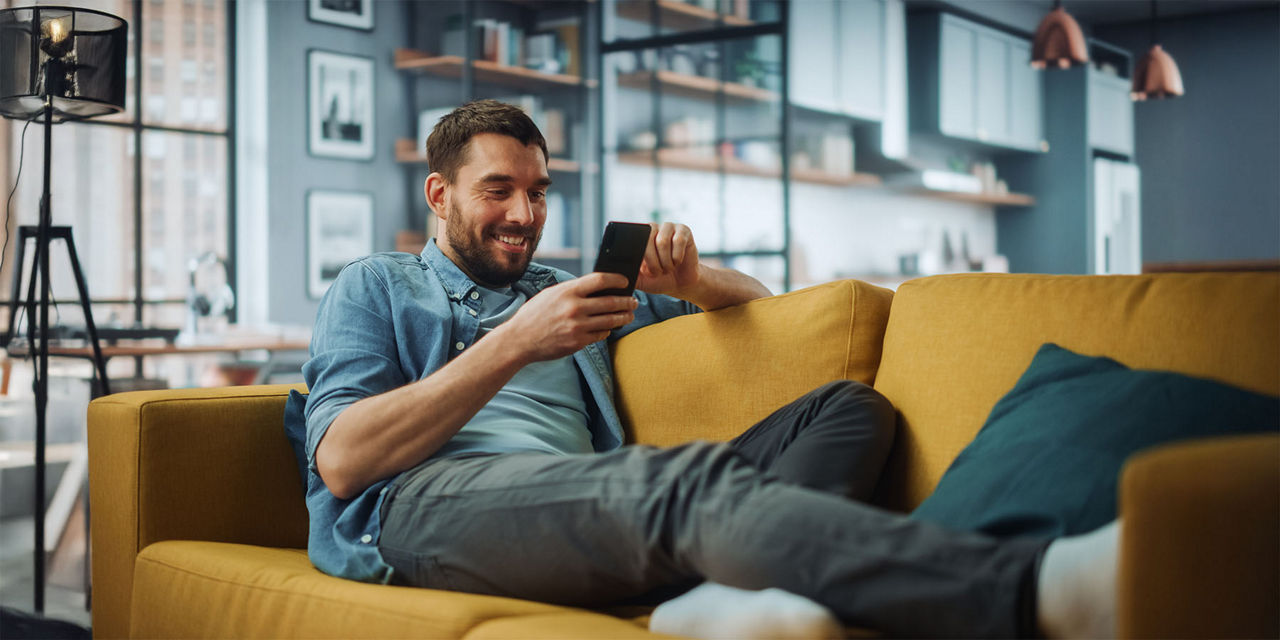 Junger Mann sitzt mit dem Smartphone in der Hand auf dem Sofa