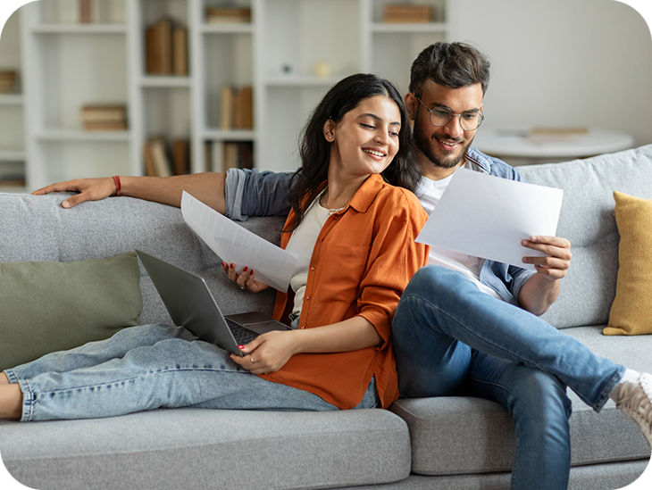 Mann und Frau auf Sofa schauen auf Unterlagen zur Vorsorge