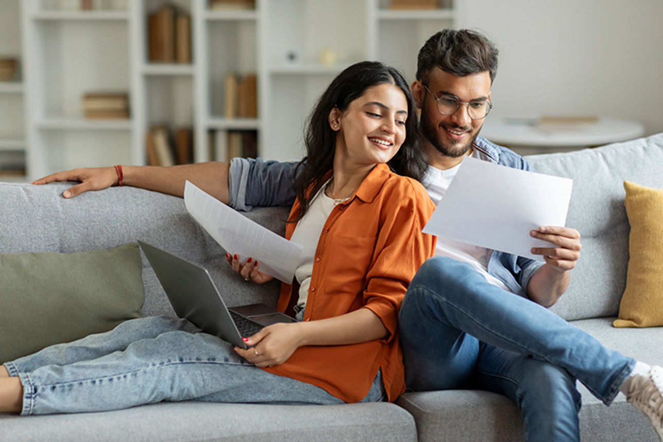 Mann und Frau auf Sofa schauen auf Unterlagen zur Vorsorge