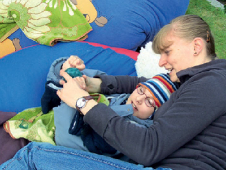 Betreuerin und Junge liegen dick eingepackt draußen und kuscheln