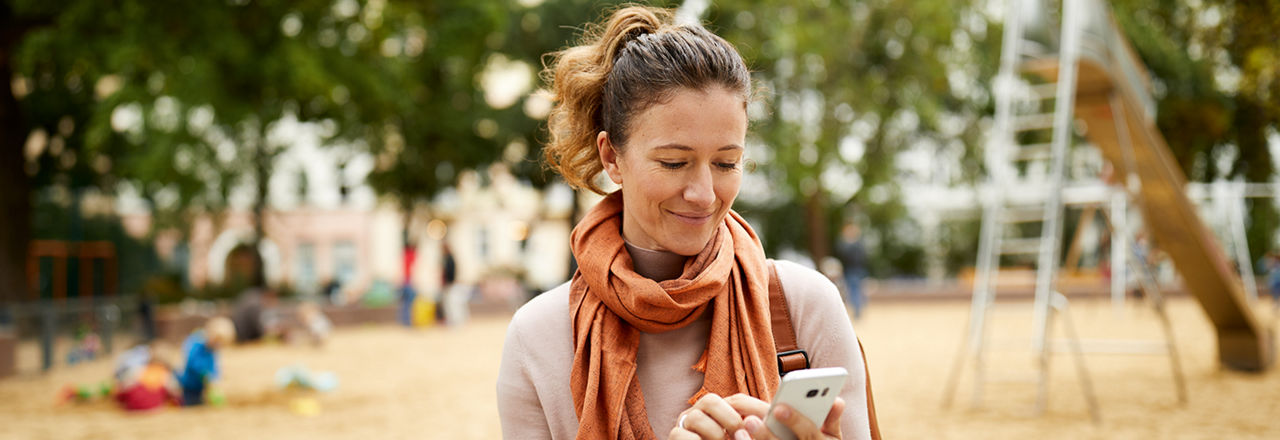 Frau mit Handy in der Hand auf dem Spielplatz