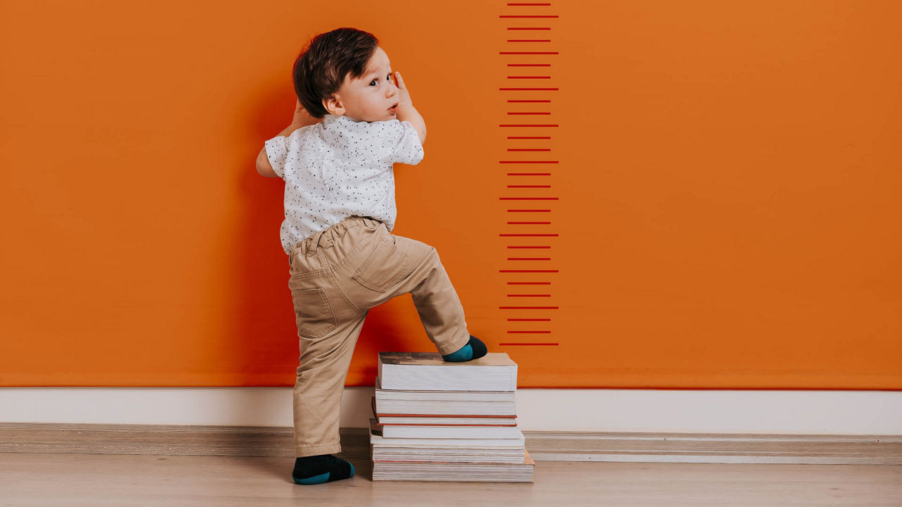 Kleiner Junge klettert auf Bücherstapel, um seine Größe zu messen.